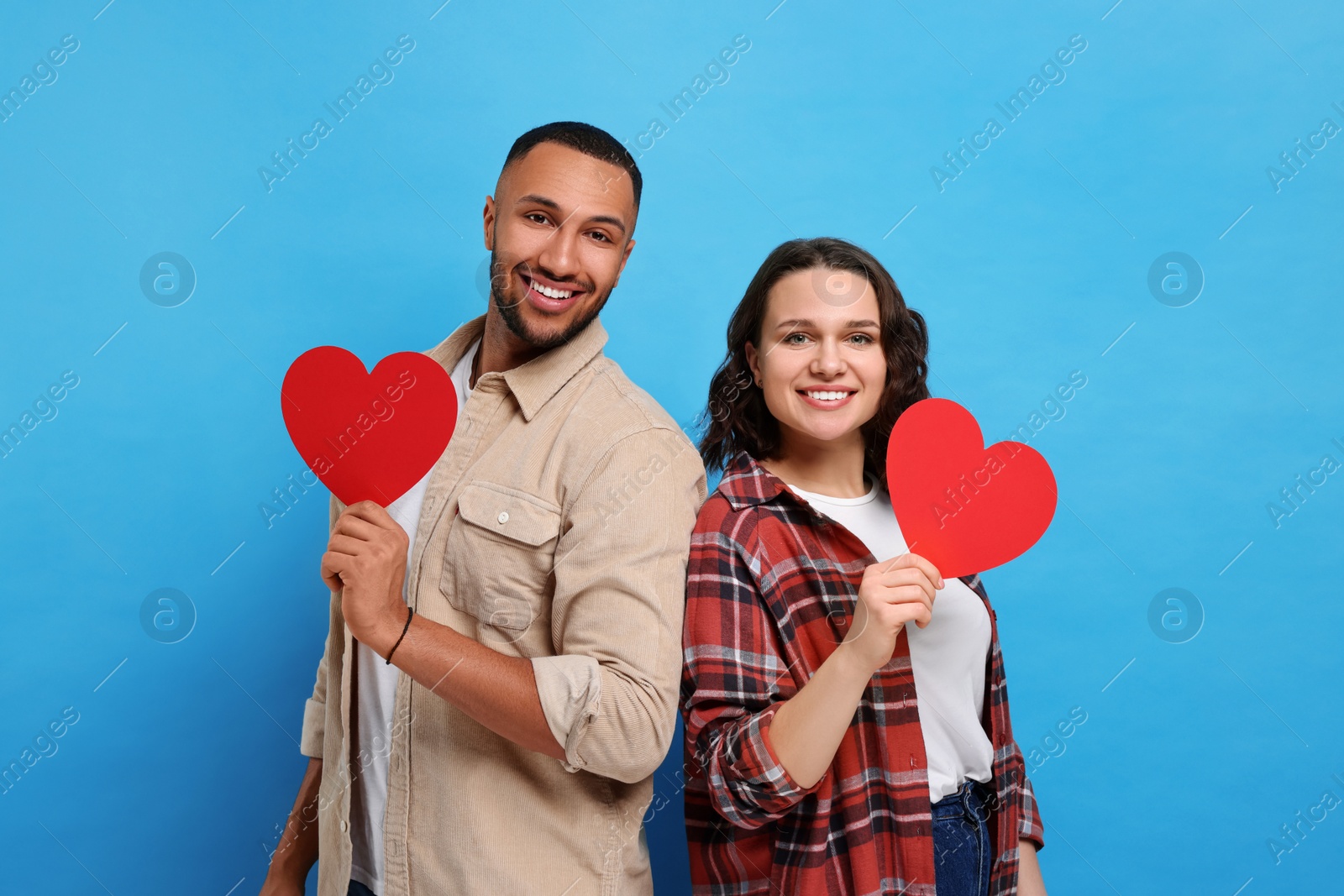 Photo of Lovely couple with red paper hearts on light blue background. Valentine's day celebration