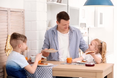 Photo of Father and cute little children having breakfast with tasty toasted bread at table