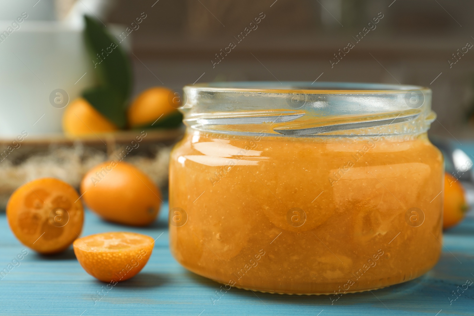 Photo of Delicious kumquat jam in jar on light blue wooden table, closeup