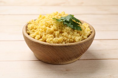 Photo of Tasty millet porridge and parsley in bowl on light wooden table, closeup