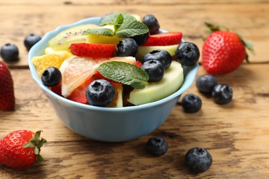 Photo of Tasty fruit salad in bowl on wooden table, closeup