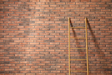 Modern wooden ladder near brick wall. Space for text
