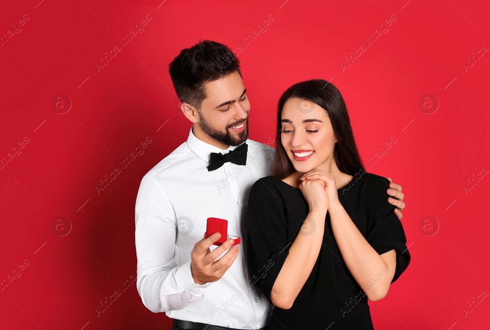 Photo of Man with engagement ring making marriage proposal to girlfriend on red background