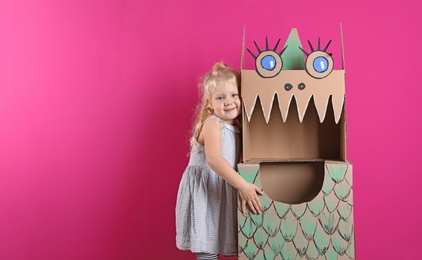 Photo of Cute little girl playing with cardboard dragon on color background. Space for text