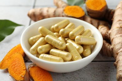 Photo of Turmeric roots and pills on light tiled table, closeup