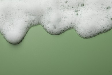 Photo of Fluffy soap foam on green background, top view. Space for text