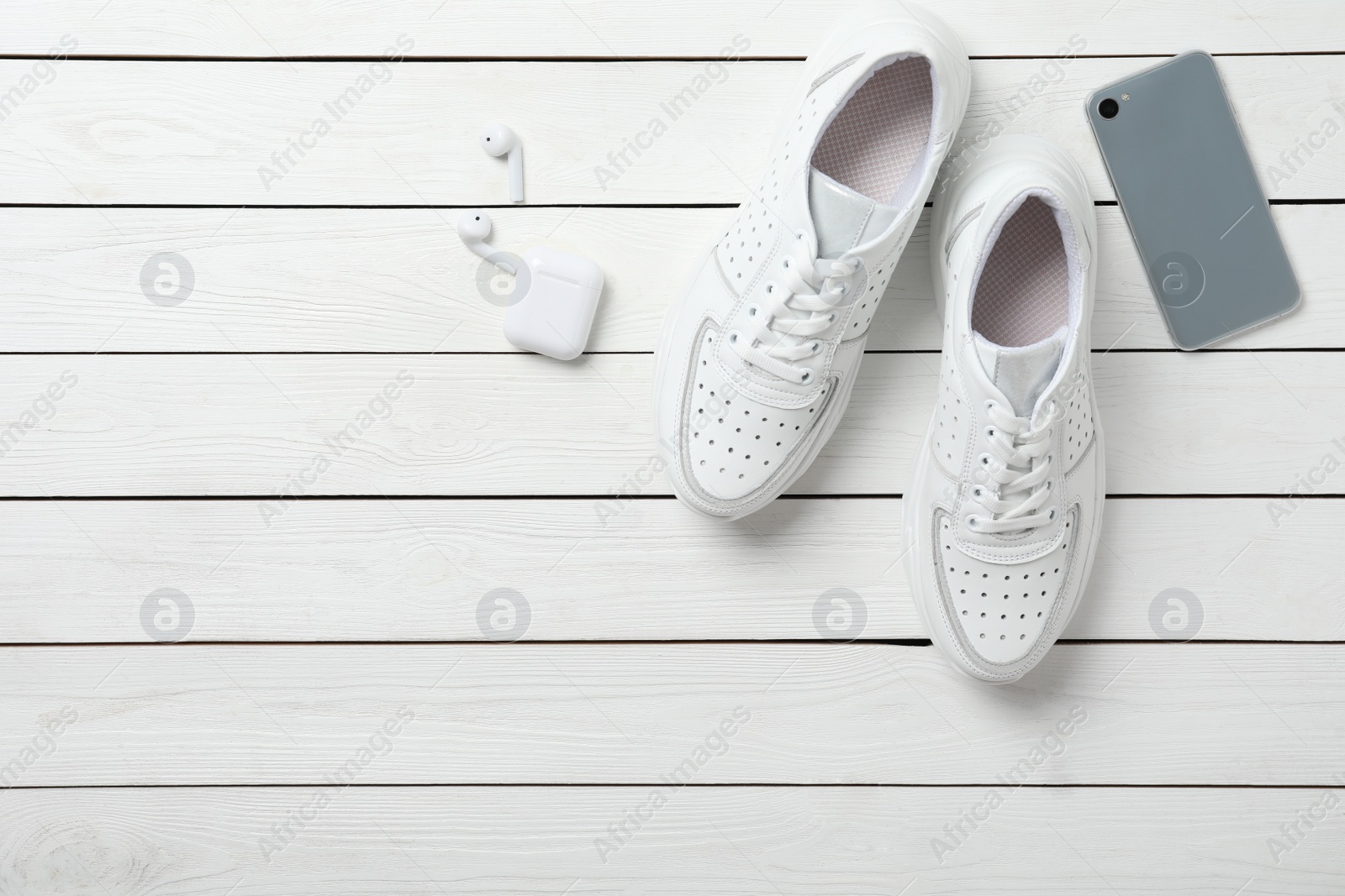 Photo of Pair of stylish shoes, modern smartphone and wireless earphones on white wooden table, flat lay. Space for text