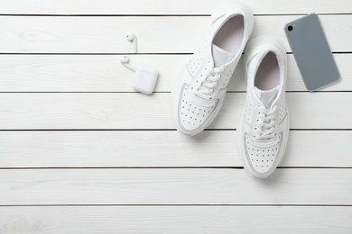 Pair of stylish shoes, modern smartphone and wireless earphones on white wooden table, flat lay. Space for text