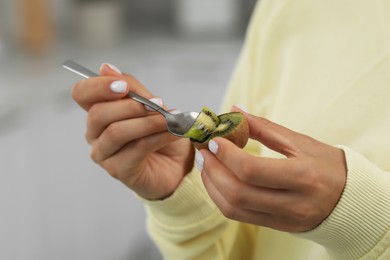 Woman eating kiwi with spoon on blurred background, closeup