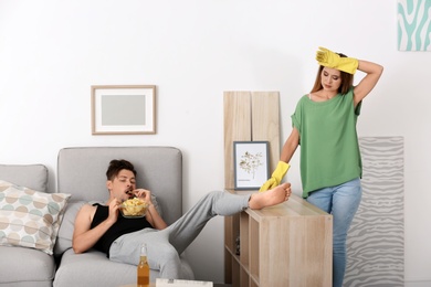 Photo of Lazy husband lying on sofa and his wife cleaning at home