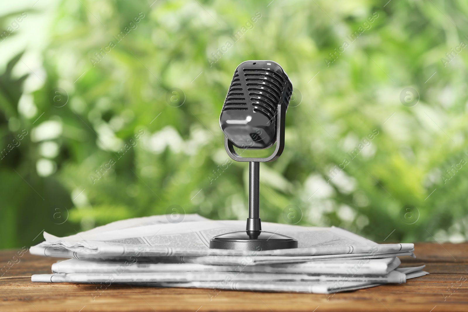 Photo of Newspapers and vintage microphone on wooden table against blurred green background. Journalist's work