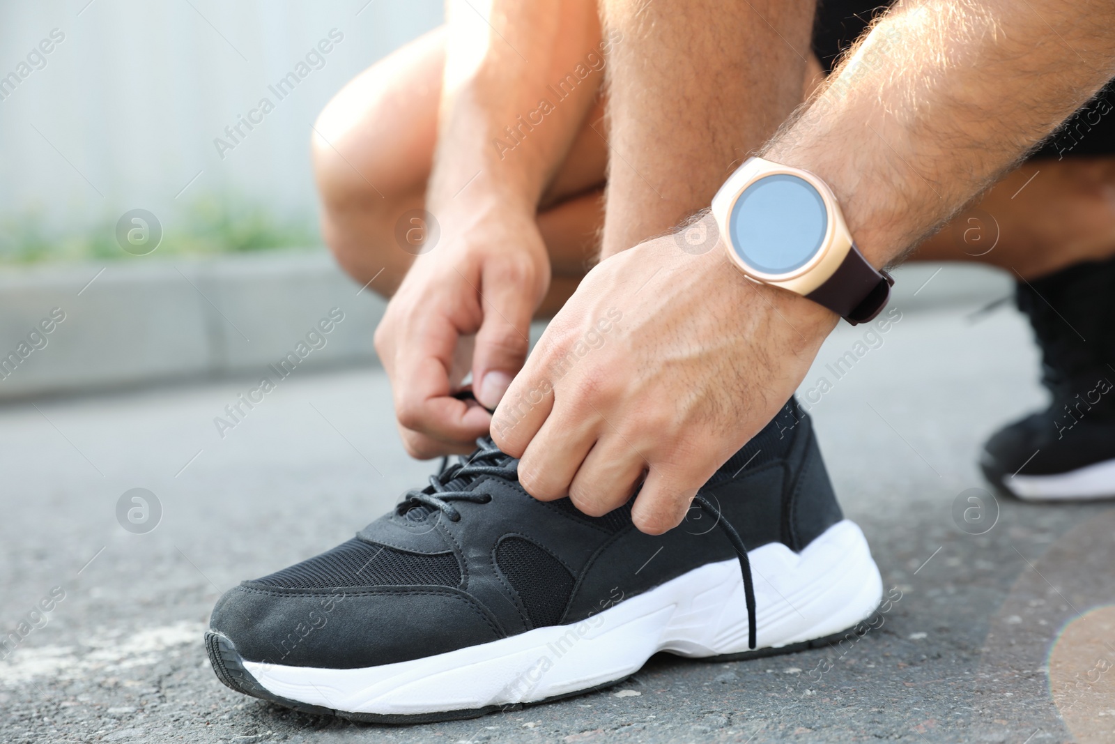 Photo of Man with fitness tracker tying shoelaces outdoors, closeup