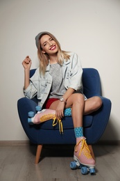 Young woman with retro roller skates in armchair against light wall