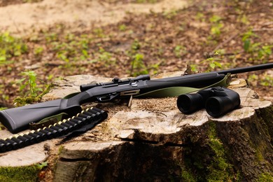 Hunting rifle, cartridges and binoculars on tree stump outdoors