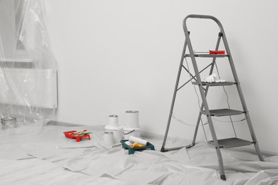 Photo of Metallic folding ladder and painting tools indoors, space for text