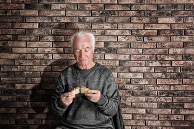 Photo of Poor elderly man with bread near brick wall