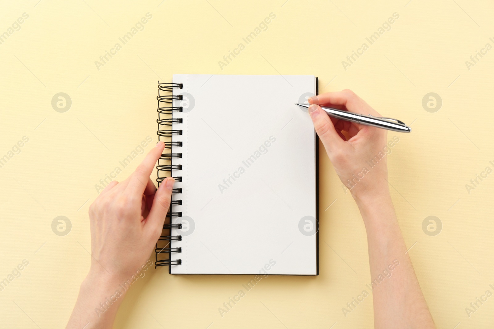 Photo of Woman writing in notebook on beige background, top view