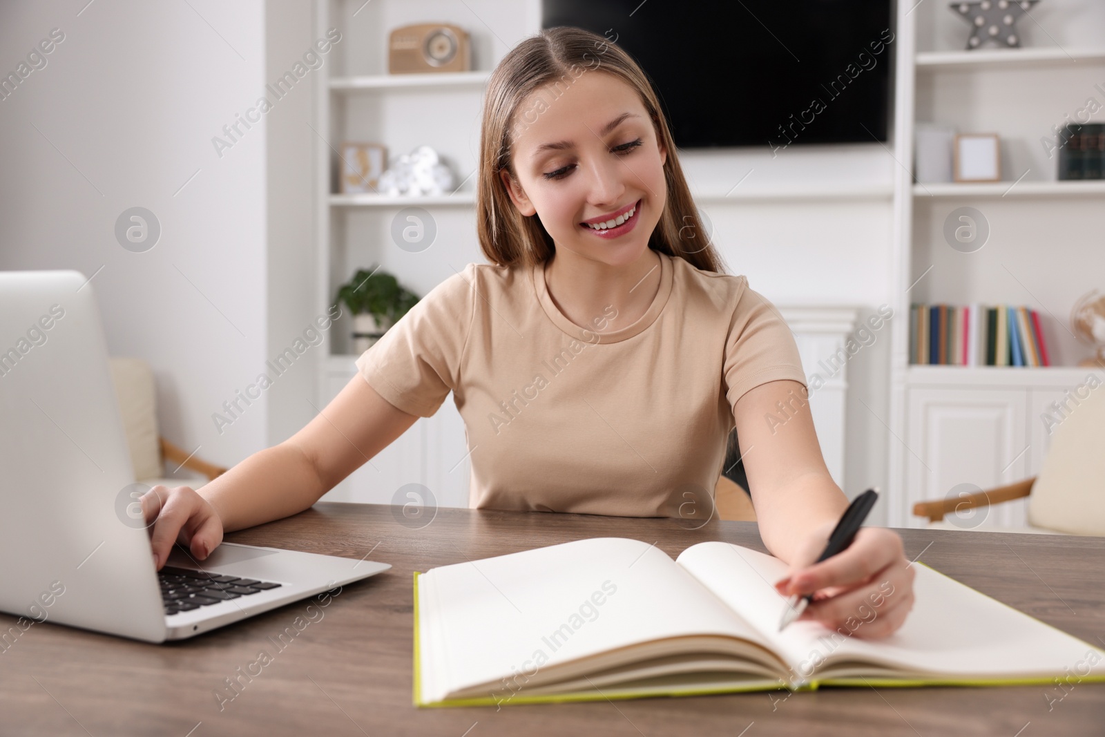 Photo of Online learning. Teenage girl writing in notebook near laptop at home