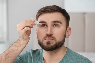 Photo of Young man using eye drops on blurred background