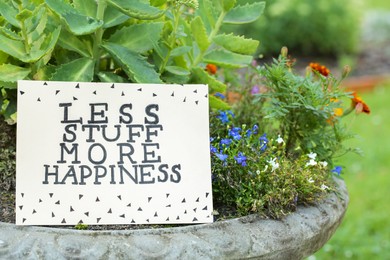 Photo of Card with phrase Less Stuff More Happiness on stone planter outdoors