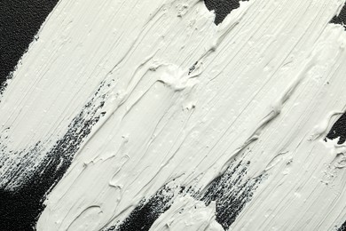 Photo of Strokes of white oil paint on black canvas, closeup