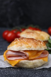 Photo of Delicious bagel with ham and cheese on dark grey textured table, closeup