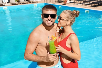 Photo of Young couple with refreshing cocktails near swimming pool at resort