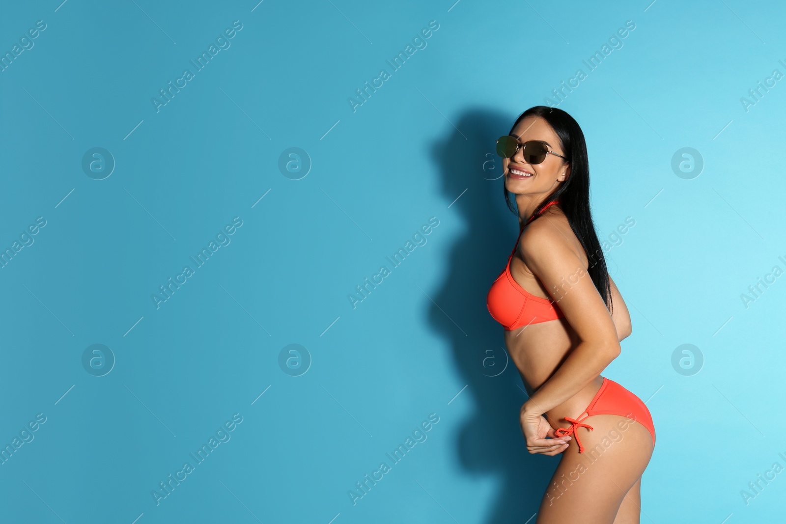 Photo of Beautiful young woman in stylish bikini with sunglasses on light blue background. Space for text