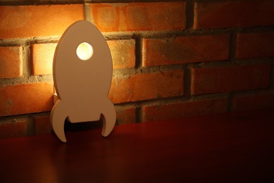 Photo of Rocket shaped night lamp on brick wall, space for text. Child's room