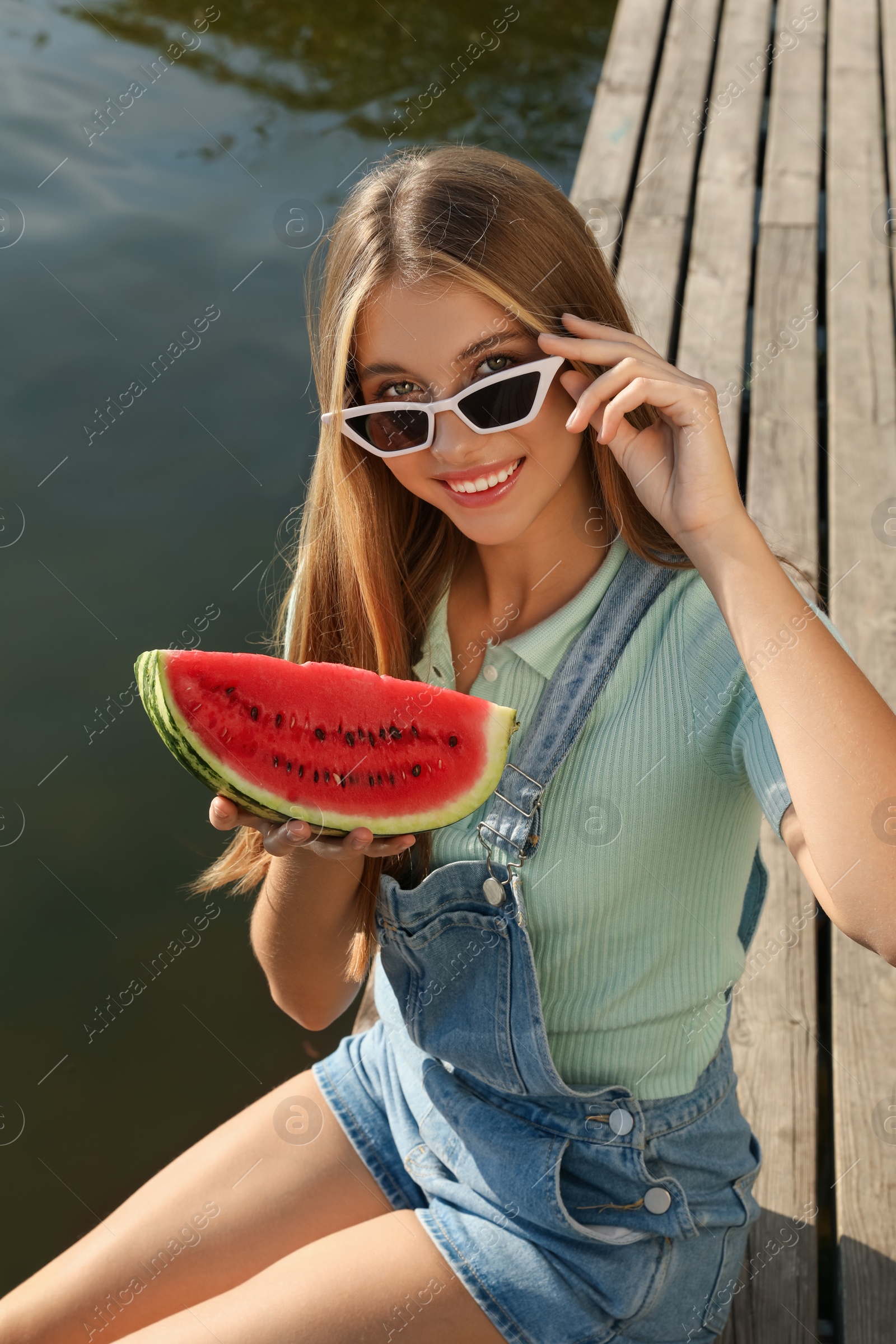 Photo of Beautiful girl with slice of watermelon on wooden pier near river