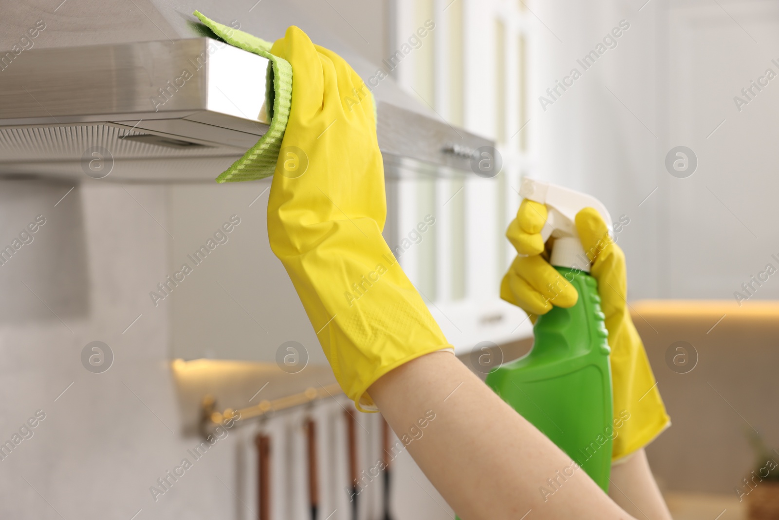 Photo of Woman with spray bottle and microfiber cloth cleaning kitchen hood indoors, closeup