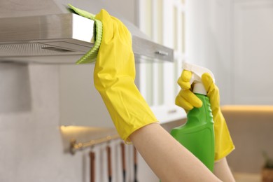 Photo of Woman with spray bottle and microfiber cloth cleaning kitchen hood indoors, closeup