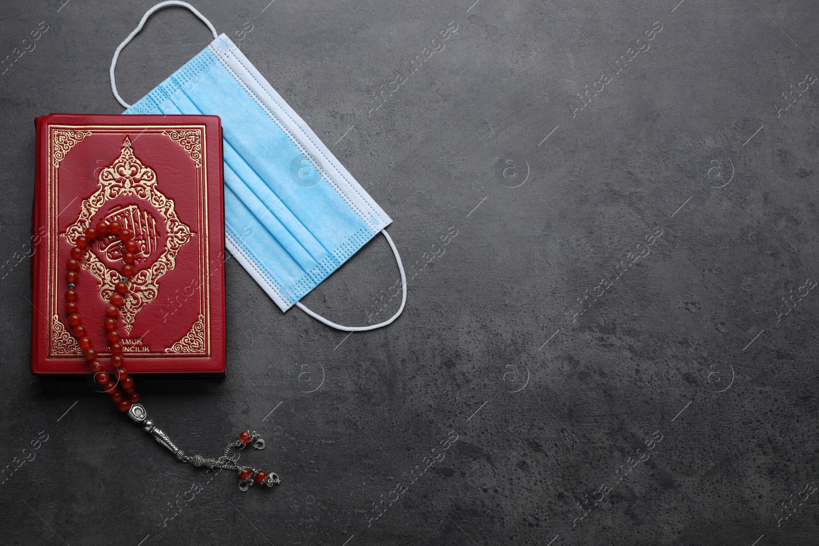 Photo of Muslim prayer beads, Quran and protective mask on grey stone table, flat lay. Space for text