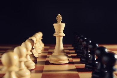 Photo of White king among pawns on chessboard against black background, closeup. Competition concept