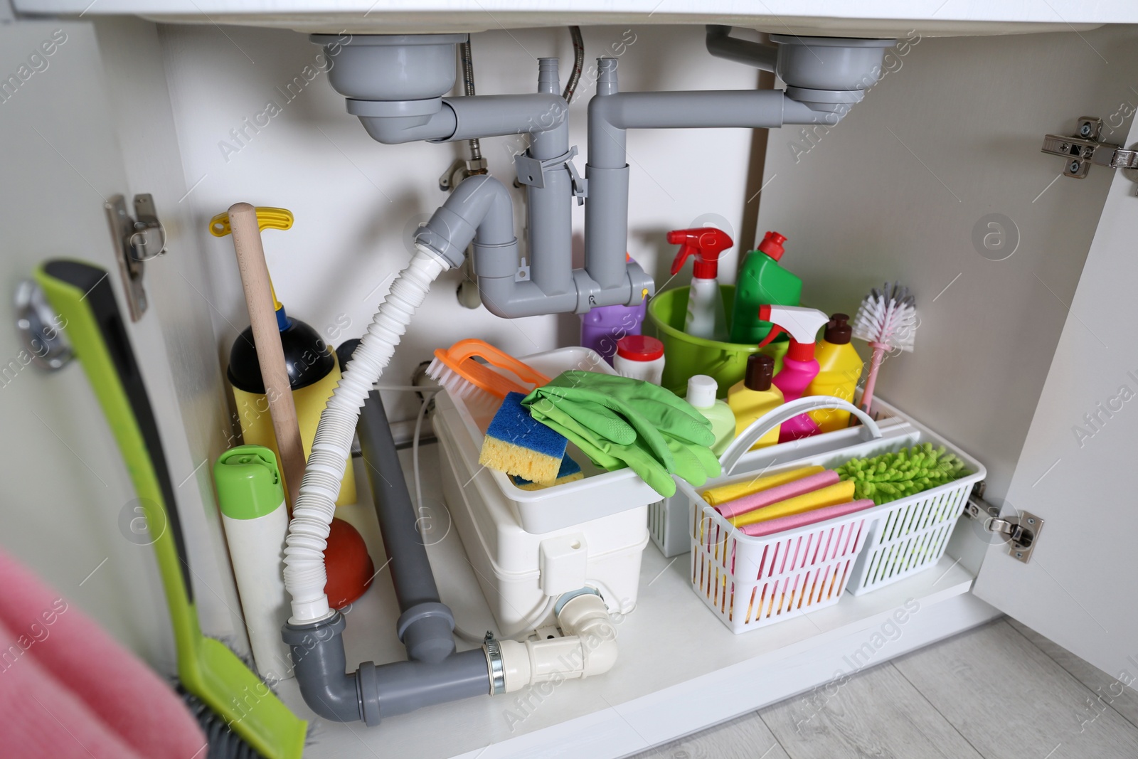 Photo of Open under sink cabinet with different cleaning supplies in kitchen