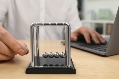 Man playing with Newton's cradle and using laptop at wooden table, closeup. Physics law of energy conservation