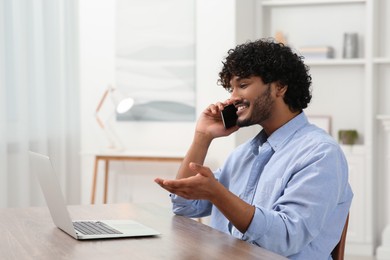 Handsome smiling man talking on smartphone in room, space for text