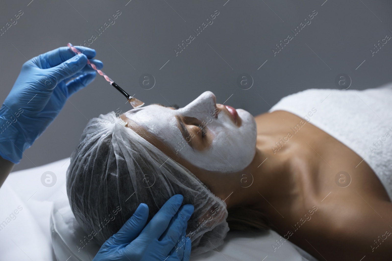 Photo of Cosmetologist applying mask on client's face in spa salon