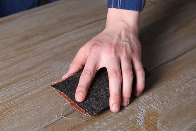 Man polishing wooden table with sandpaper, closeup