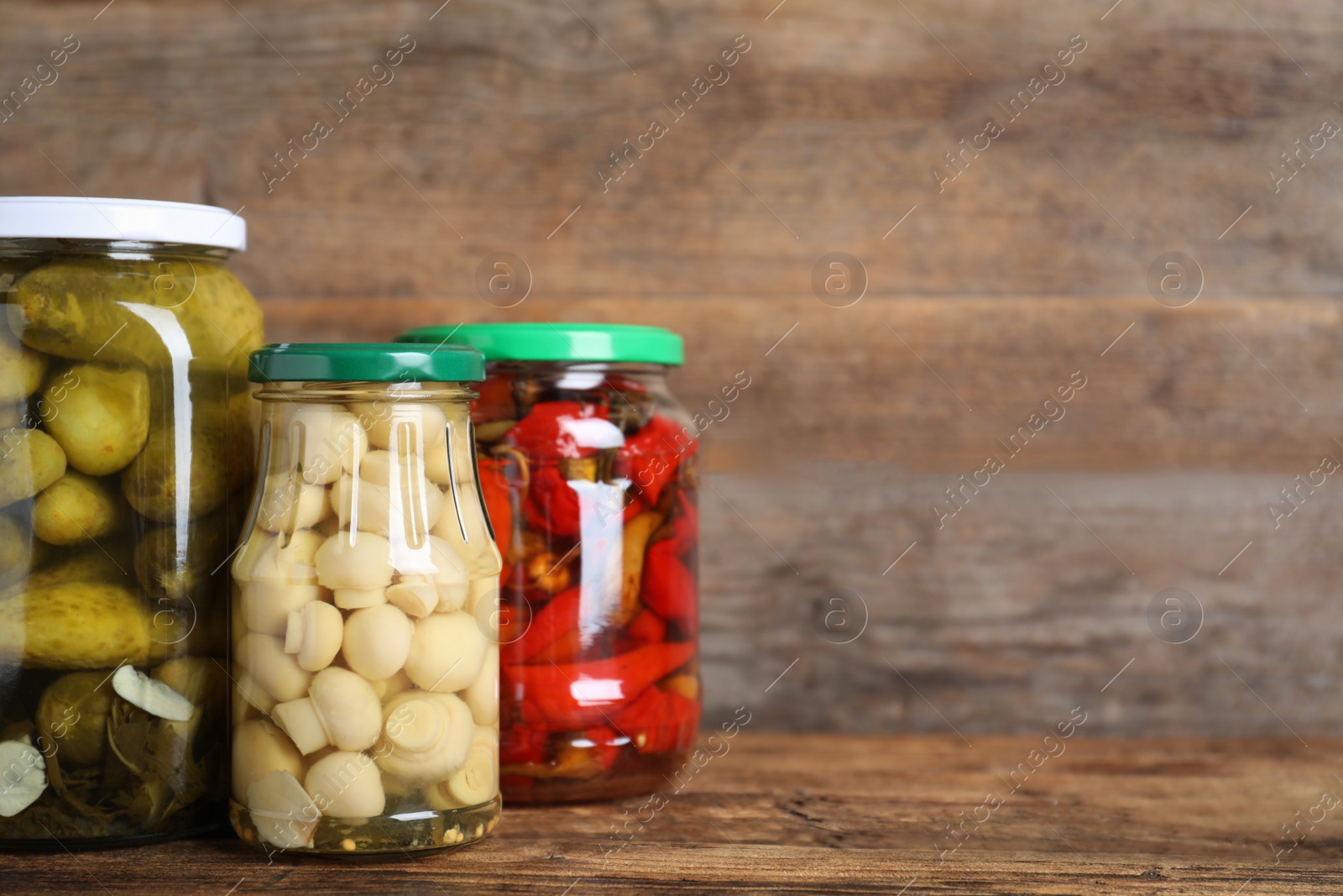 Photo of Glass jars with different pickled vegetables on wooden table. Space for text