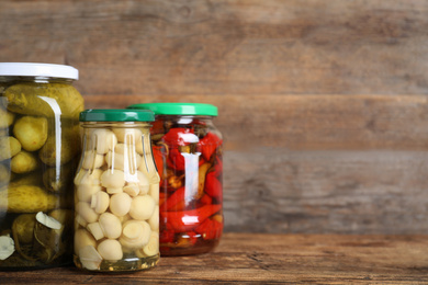 Glass jars with different pickled vegetables on wooden table. Space for text