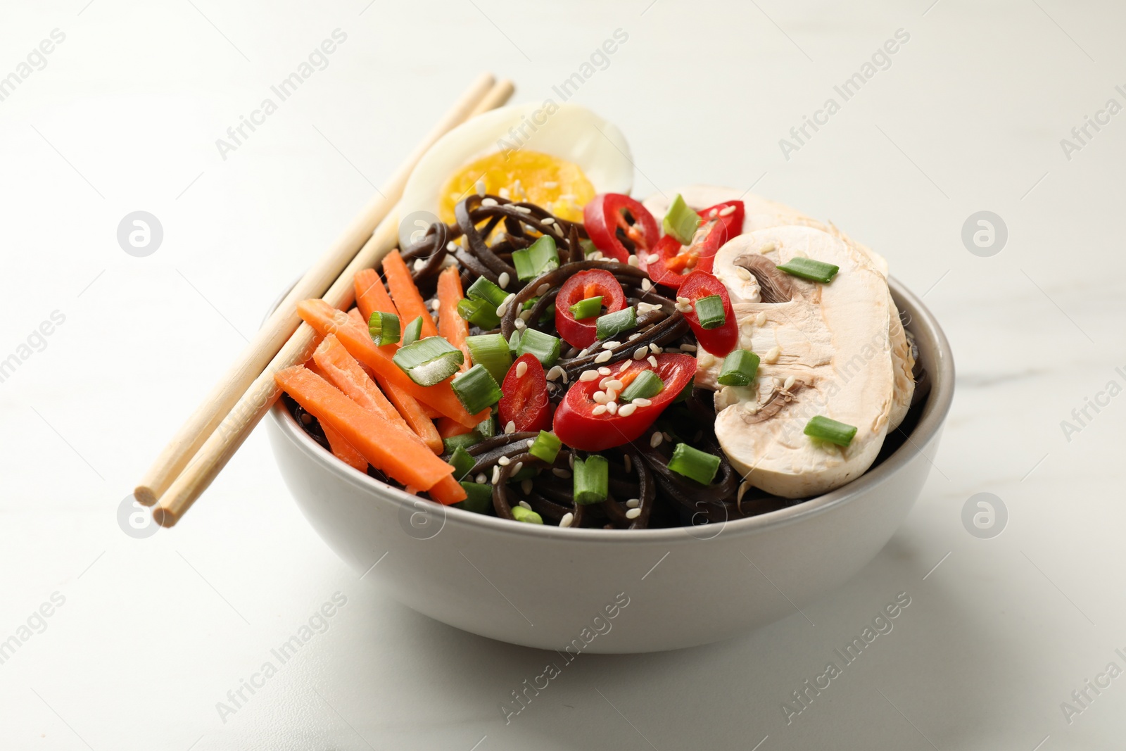 Photo of Tasty buckwheat noodles (soba) with chili pepper, egg, carrot, mushrooms and chopsticks on white marble table, closeup