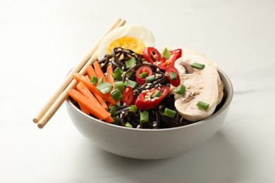 Photo of Tasty buckwheat noodles (soba) with chili pepper, egg, carrot, mushrooms and chopsticks on white marble table, closeup