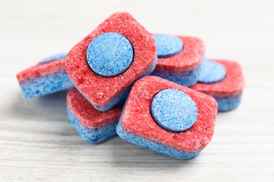 Many dishwasher detergent tablets on white wooden table, closeup