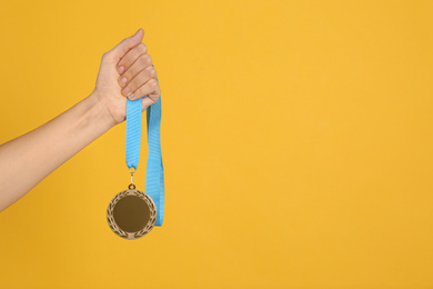 Photo of Woman holding bronze medal on yellow background, closeup. Space for design
