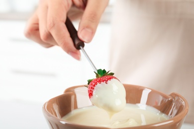 Woman dipping ripe strawberry into bowl with white chocolate fondue, closeup