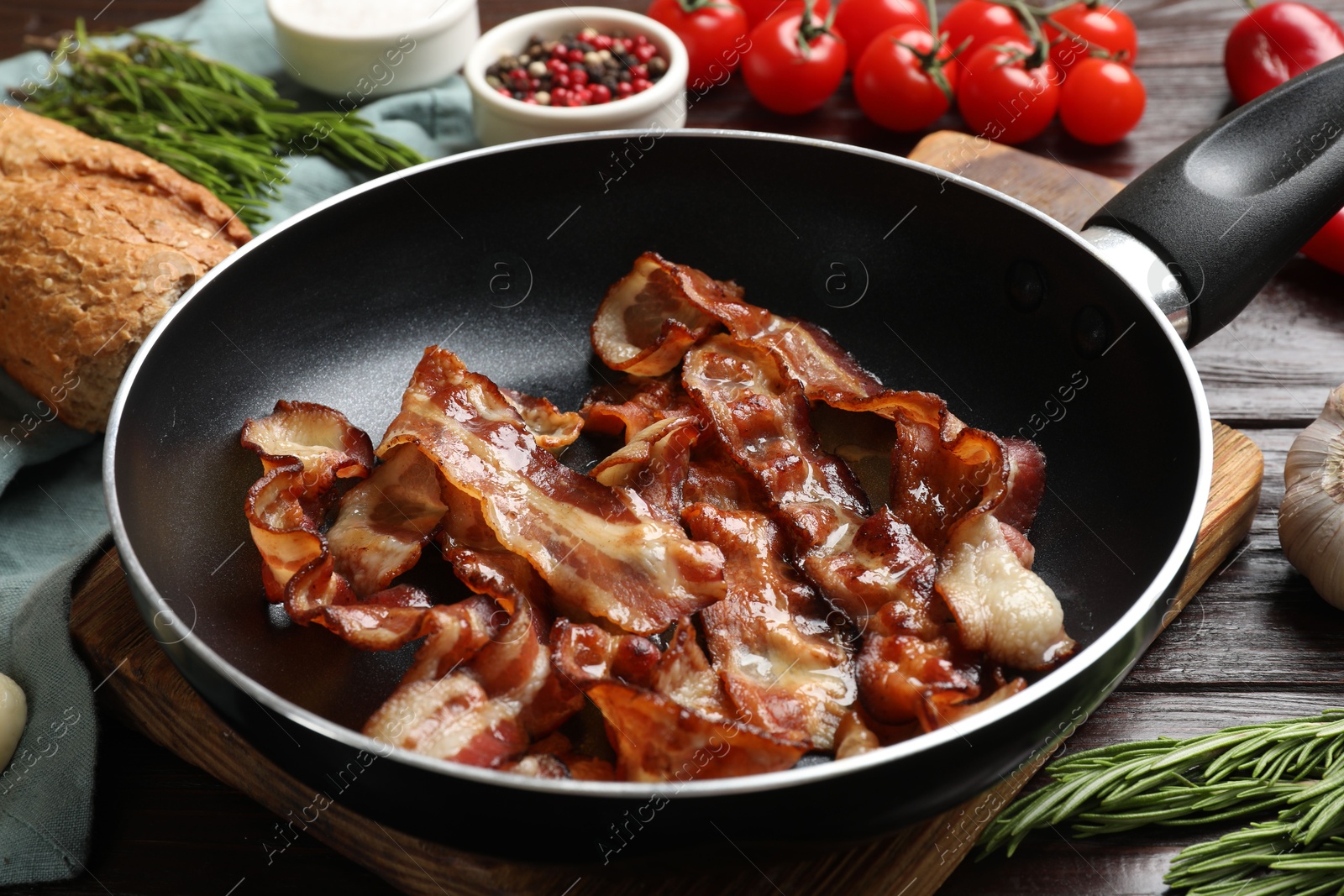 Photo of Delicious bacon slices in frying pan and products on wooden table, closeup