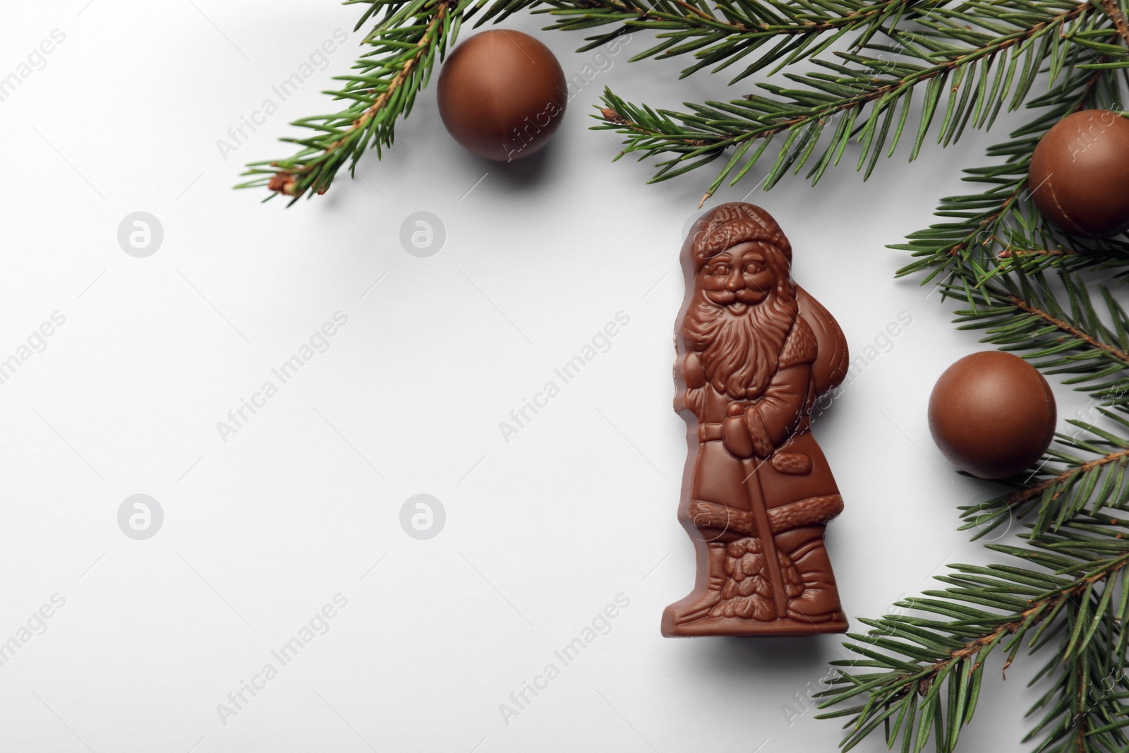 Photo of Flat lay composition with chocolate Santa Claus, fir tree twigs and sweets on white background, space for text