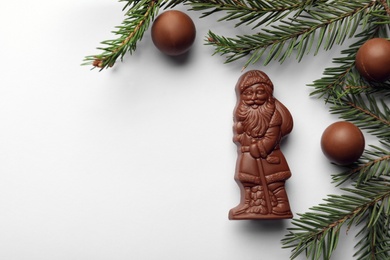 Photo of Flat lay composition with chocolate Santa Claus, fir tree twigs and sweets on white background, space for text