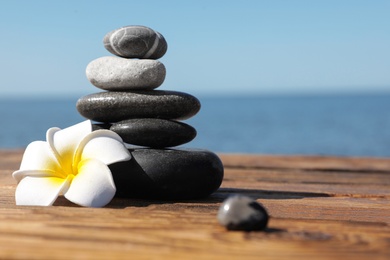 Photo of Stack of stones and flower on wooden pier near sea, space for text. Zen concept